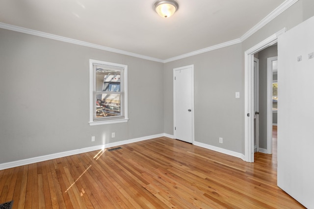 empty room with crown molding, light wood-style flooring, and baseboards