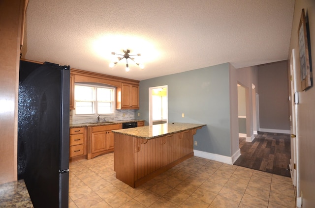 kitchen with sink, light stone counters, fridge, a kitchen breakfast bar, and decorative backsplash