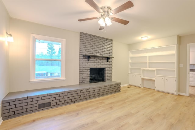 unfurnished living room featuring ceiling fan, a brick fireplace, and light hardwood / wood-style flooring