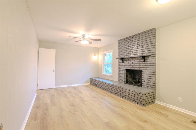 unfurnished living room featuring ceiling fan, a brick fireplace, and light wood-type flooring