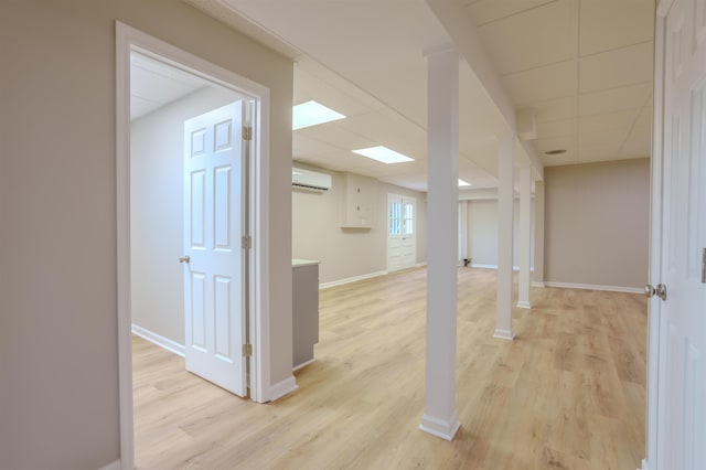 basement featuring a paneled ceiling, a wall mounted air conditioner, and light wood-type flooring