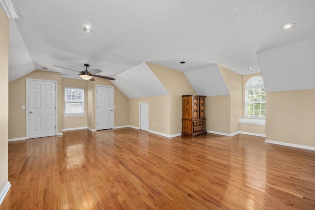 additional living space with lofted ceiling, light hardwood / wood-style flooring, ceiling fan, a textured ceiling, and a healthy amount of sunlight