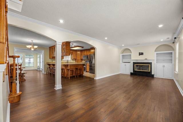 living room featuring a chandelier, a textured ceiling, built in features, and crown molding