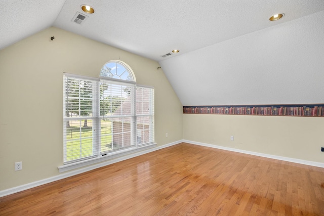 additional living space featuring hardwood / wood-style floors, a textured ceiling, and vaulted ceiling