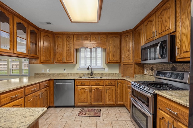 kitchen featuring a wealth of natural light, light stone countertops, sink, and appliances with stainless steel finishes