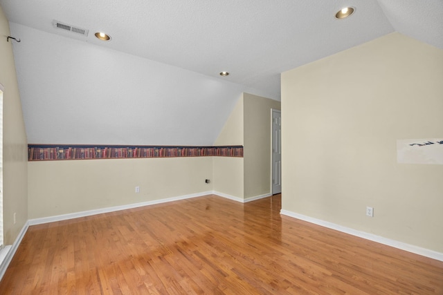 unfurnished room featuring wood-type flooring, a textured ceiling, and vaulted ceiling