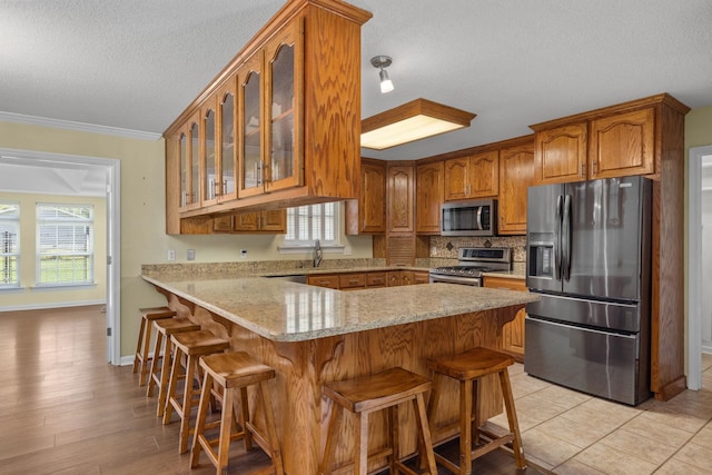 kitchen with stainless steel appliances, a kitchen breakfast bar, kitchen peninsula, a textured ceiling, and ornamental molding