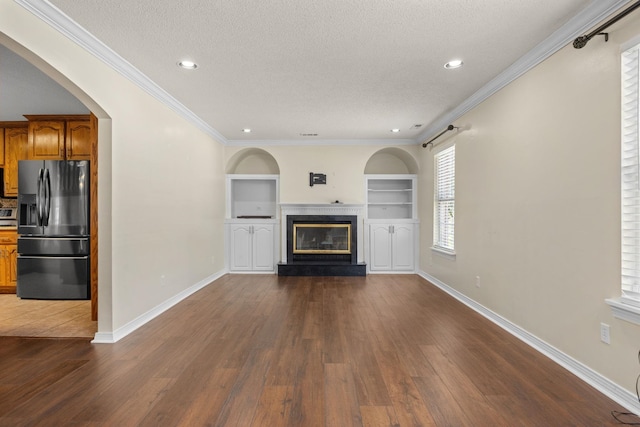 unfurnished living room with built in shelves, a textured ceiling, dark hardwood / wood-style floors, and ornamental molding