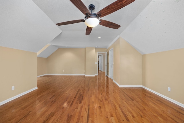 additional living space with a textured ceiling, light hardwood / wood-style flooring, ceiling fan, and vaulted ceiling