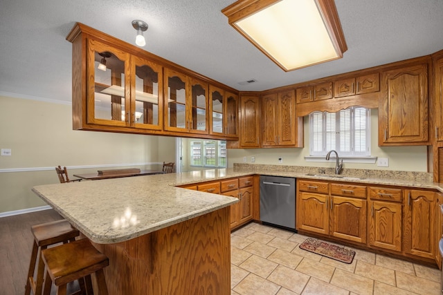 kitchen with kitchen peninsula, light stone counters, stainless steel dishwasher, a breakfast bar, and sink