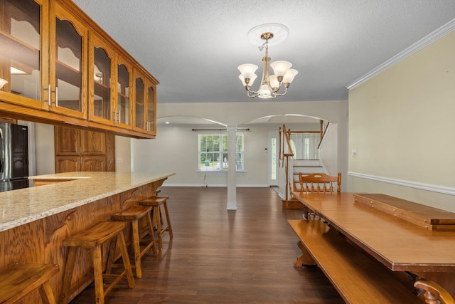 kitchen with light stone countertops, stainless steel fridge, crown molding, decorative light fixtures, and a chandelier