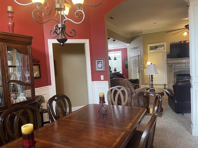 dining area featuring a premium fireplace, ornamental molding, carpet flooring, and ceiling fan with notable chandelier