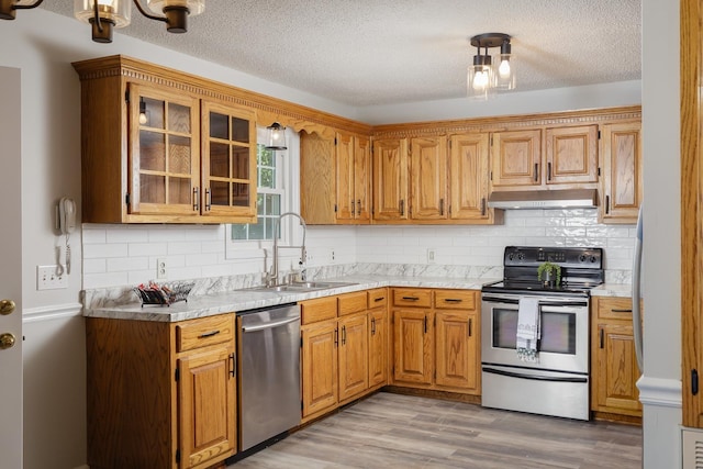 kitchen with under cabinet range hood, appliances with stainless steel finishes, light countertops, and a sink