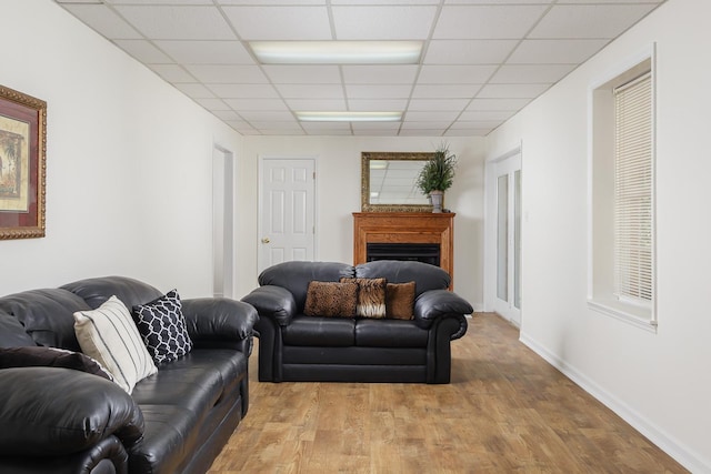 living room featuring a fireplace, wood finished floors, a paneled ceiling, and baseboards