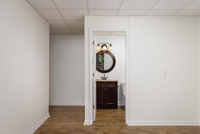 corridor with wood finished floors, a paneled ceiling, and baseboards