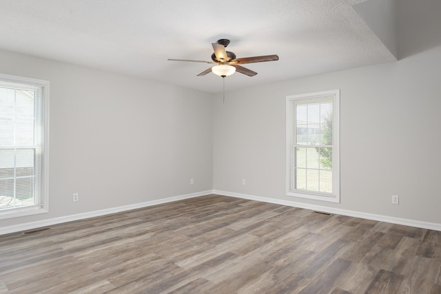 unfurnished room with a ceiling fan, wood finished floors, visible vents, and baseboards