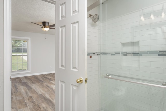 bathroom with baseboards, a tile shower, a textured ceiling, and wood finished floors