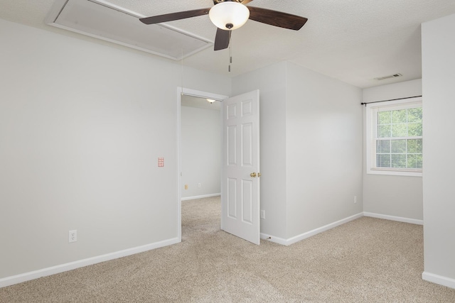 carpeted empty room featuring a ceiling fan, attic access, visible vents, and baseboards