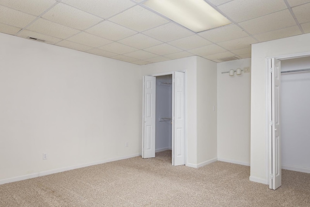 unfurnished bedroom featuring light carpet, visible vents, a paneled ceiling, and baseboards