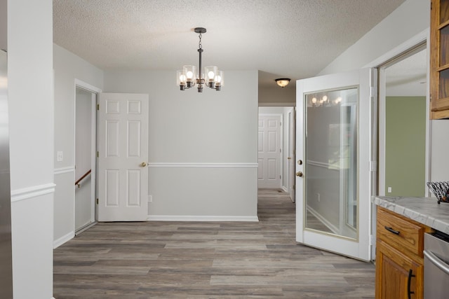 unfurnished dining area featuring a notable chandelier, a textured ceiling, and wood finished floors