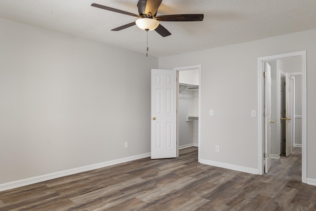 unfurnished bedroom with baseboards, dark wood-type flooring, a spacious closet, a textured ceiling, and a closet