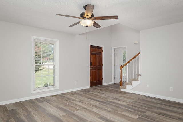 empty room featuring lofted ceiling, stairway, a textured ceiling, and wood finished floors