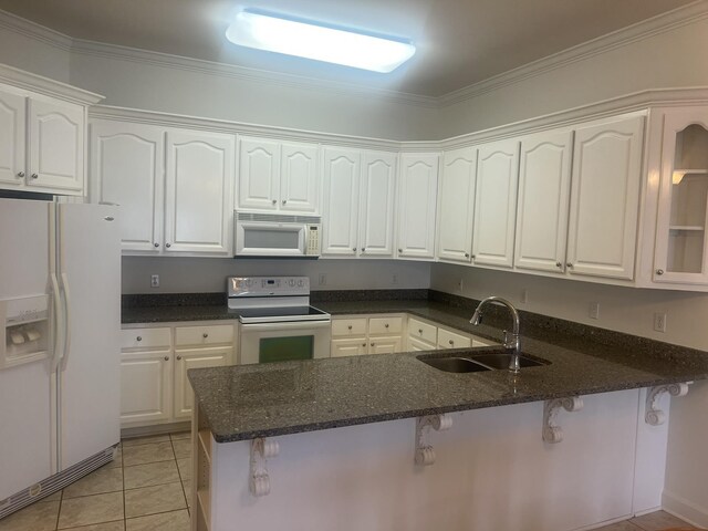  - kitchen with white appliances, white cabinetry, a peninsula, dark stone countertops, and a breakfast bar