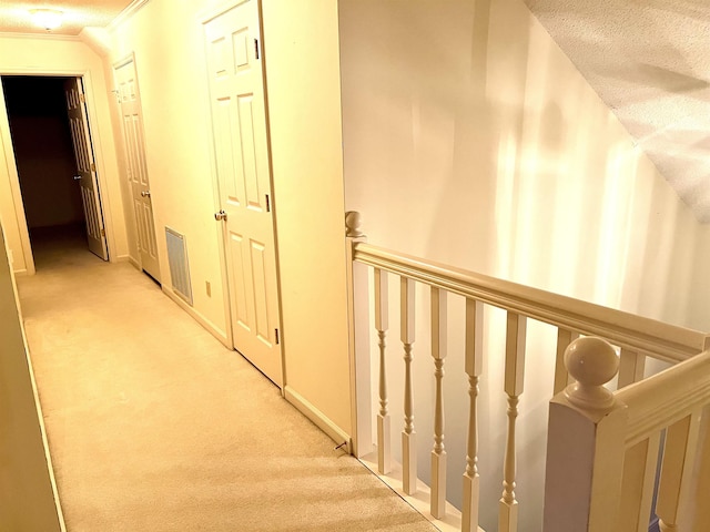 corridor featuring light colored carpet, ornamental molding, and a textured ceiling