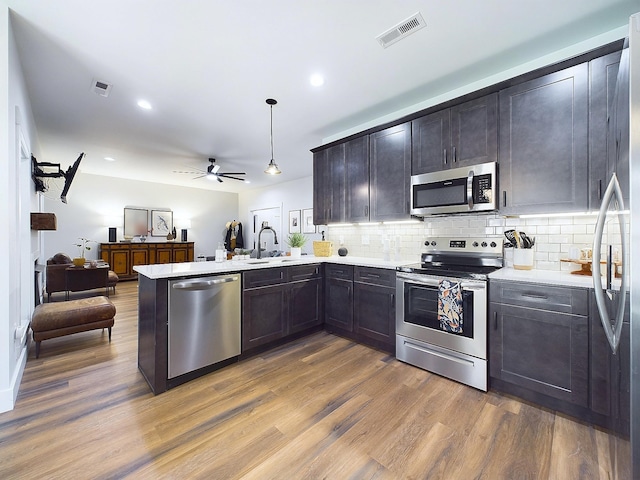 kitchen with sink, stainless steel appliances, kitchen peninsula, wood-type flooring, and decorative light fixtures