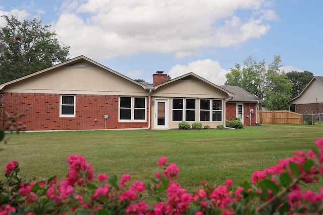 back of property featuring a yard, a chimney, fence, and brick siding