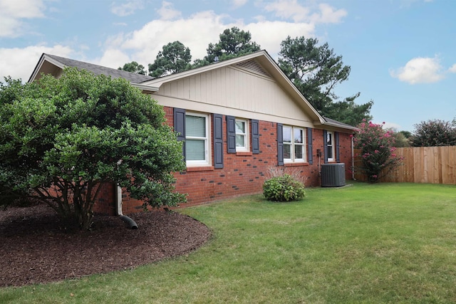 view of side of property featuring brick siding, a lawn, cooling unit, and fence