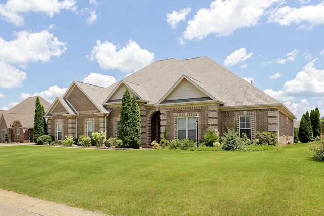  - view of front facade featuring brick siding, a front yard, and roof with shingles