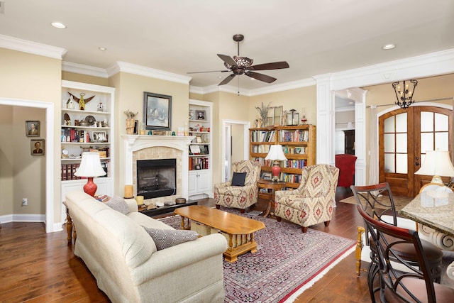  - living room with a ceiling fan, dark wood-style flooring, a tiled fireplace, ornamental molding, and built in features
