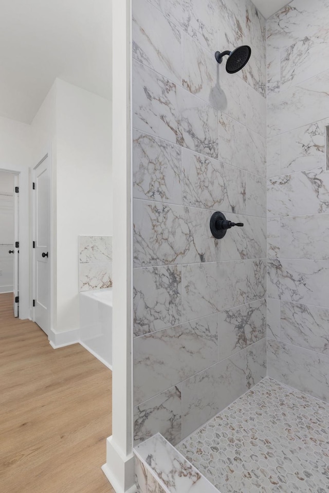 full bathroom with wood finished floors, tiled shower, a bath, and baseboards