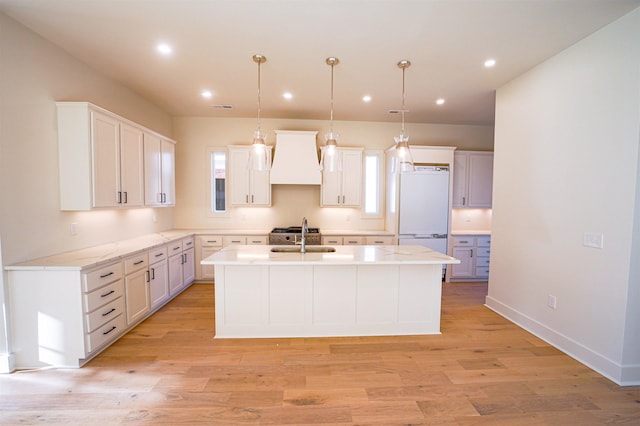 kitchen with white cabinetry, hanging light fixtures, white refrigerator, a center island with sink, and custom exhaust hood