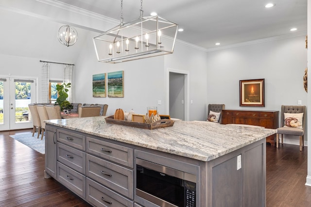 kitchen with french doors, light stone counters, stainless steel microwave, a center island, and hanging light fixtures