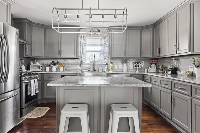 kitchen featuring gray cabinetry, a center island, stainless steel appliances, and a breakfast bar area