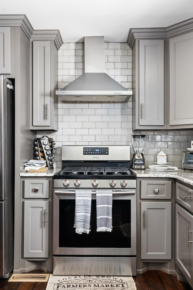 kitchen with gray cabinetry, wall chimney exhaust hood, decorative backsplash, and stainless steel appliances