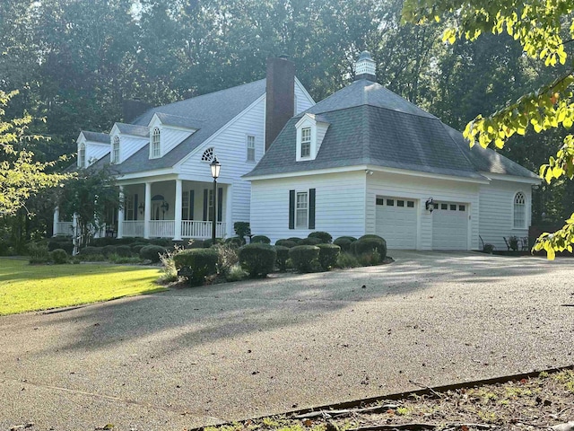 new england style home featuring covered porch, a garage, and a front lawn