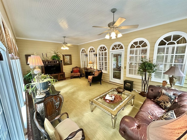 carpeted living room with wooden walls, ceiling fan, and ornamental molding