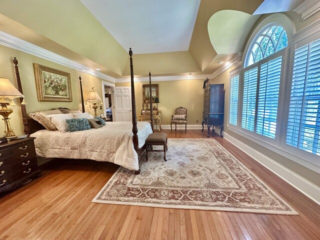 bedroom with hardwood / wood-style floors, a raised ceiling, crown molding, and multiple windows