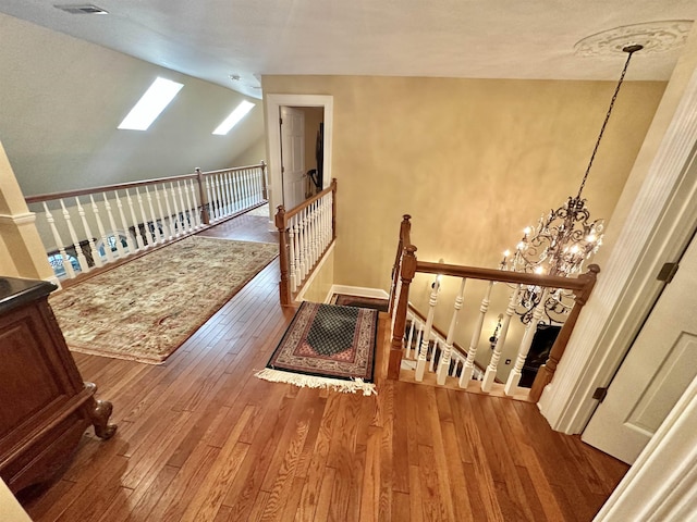 stairway featuring hardwood / wood-style flooring, vaulted ceiling with skylight, and an inviting chandelier