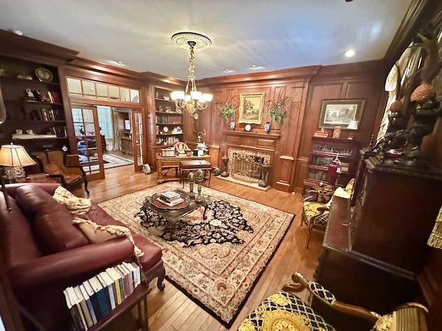 living room featuring built in shelves, hardwood / wood-style flooring, ornamental molding, and a notable chandelier