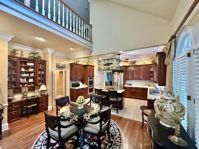 dining area featuring a towering ceiling, light wood-type flooring, ceiling fan, and crown molding