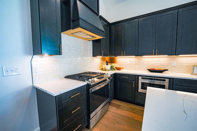 kitchen featuring decorative backsplash, premium range hood, light stone counters, gas stove, and dark wood-type flooring