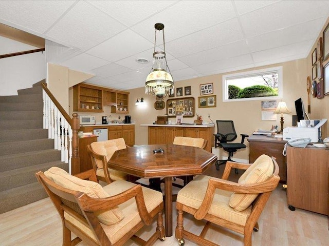 dining area featuring light wood-style floors, stairs, a paneled ceiling, and bar