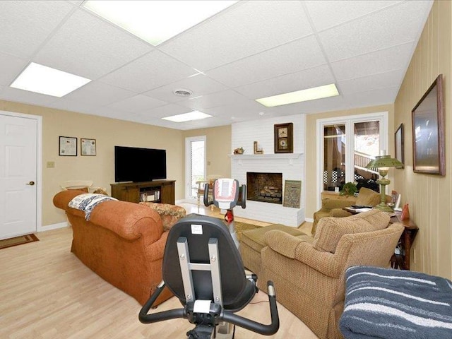 living room featuring a wealth of natural light, light wood finished floors, a brick fireplace, visible vents, and a drop ceiling