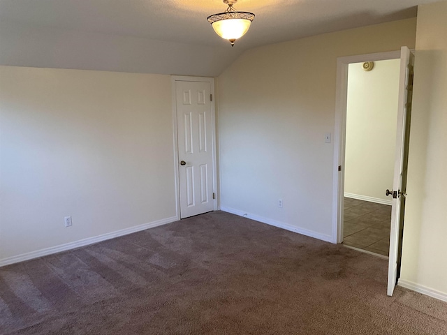 unfurnished room featuring vaulted ceiling and dark carpet