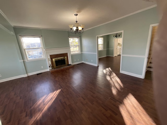 unfurnished living room with crown molding, dark wood-type flooring, a notable chandelier, and a healthy amount of sunlight