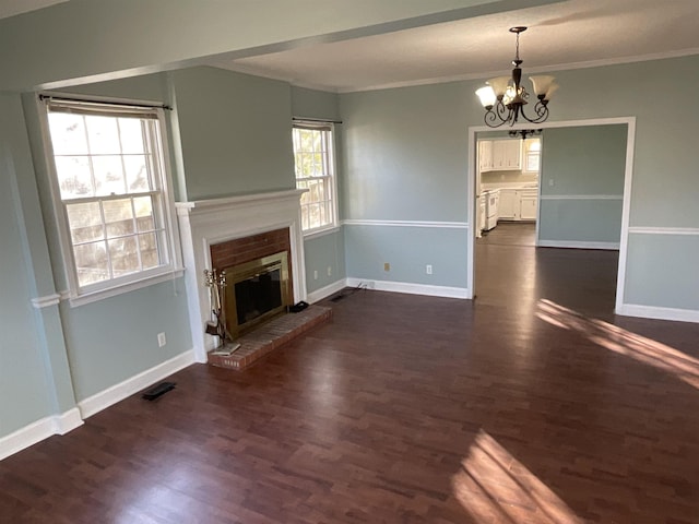 unfurnished living room with an inviting chandelier, ornamental molding, dark hardwood / wood-style floors, and a brick fireplace